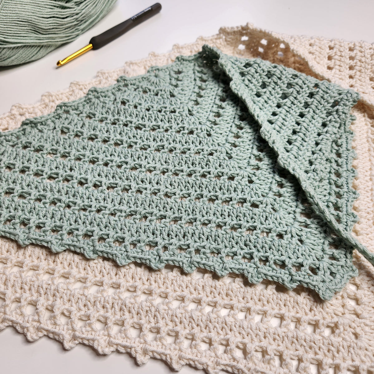 Crocheted green blanket with a crochet hook on a textured surface