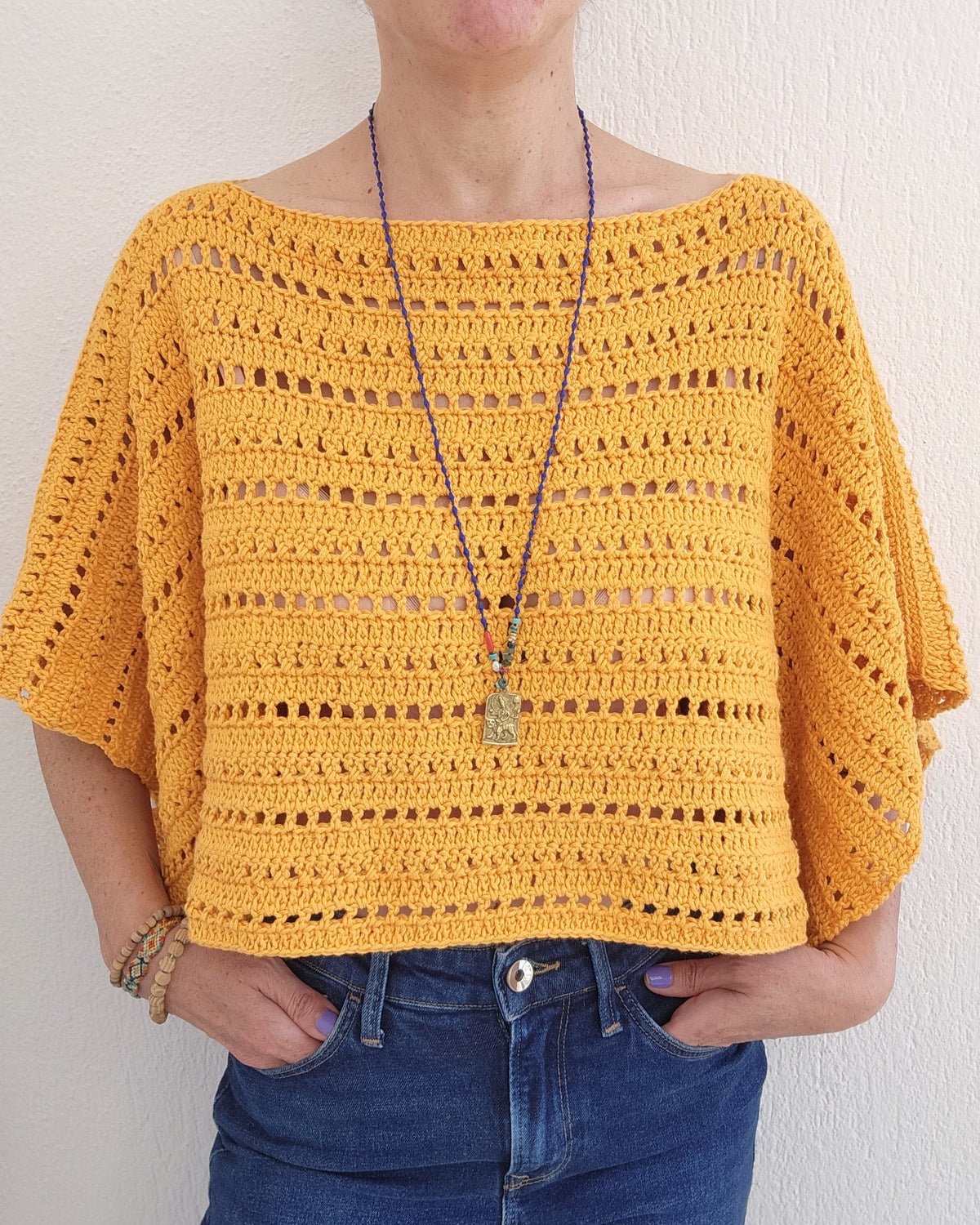 Person wearing a yellow crochet top with a plain background